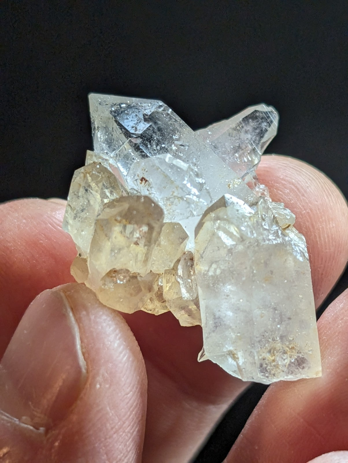 A translucent, multi-faceted quartz crystal cluster with clear and golden-yellow hues held gently in fingers.