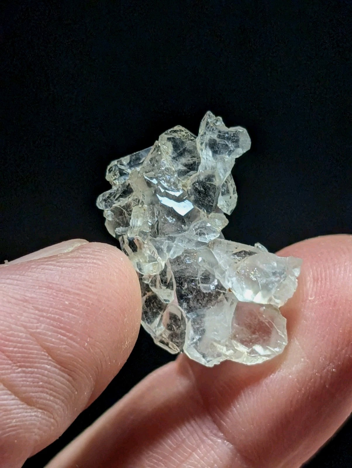 A translucent, clear quartz crystal cluster held gently between fingers.