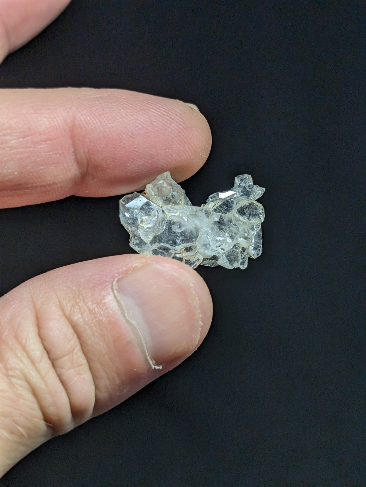 A clear, faceted crystal cluster held between fingers.