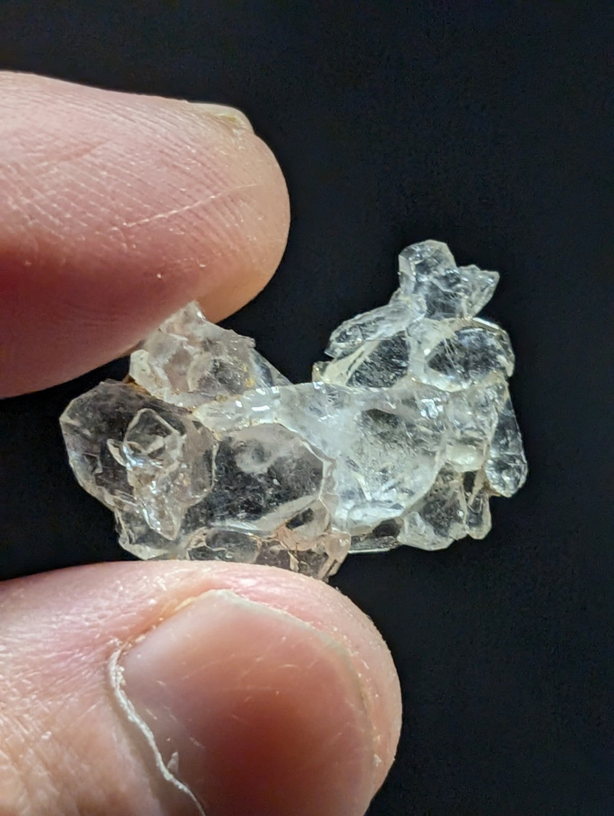 A cluster of clear, translucent glass crystals held between fingers.