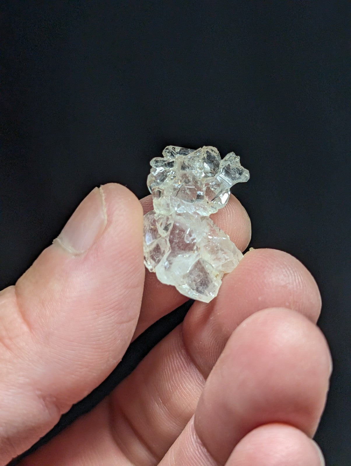 A cluster of clear, faceted quartz crystals held between fingers.