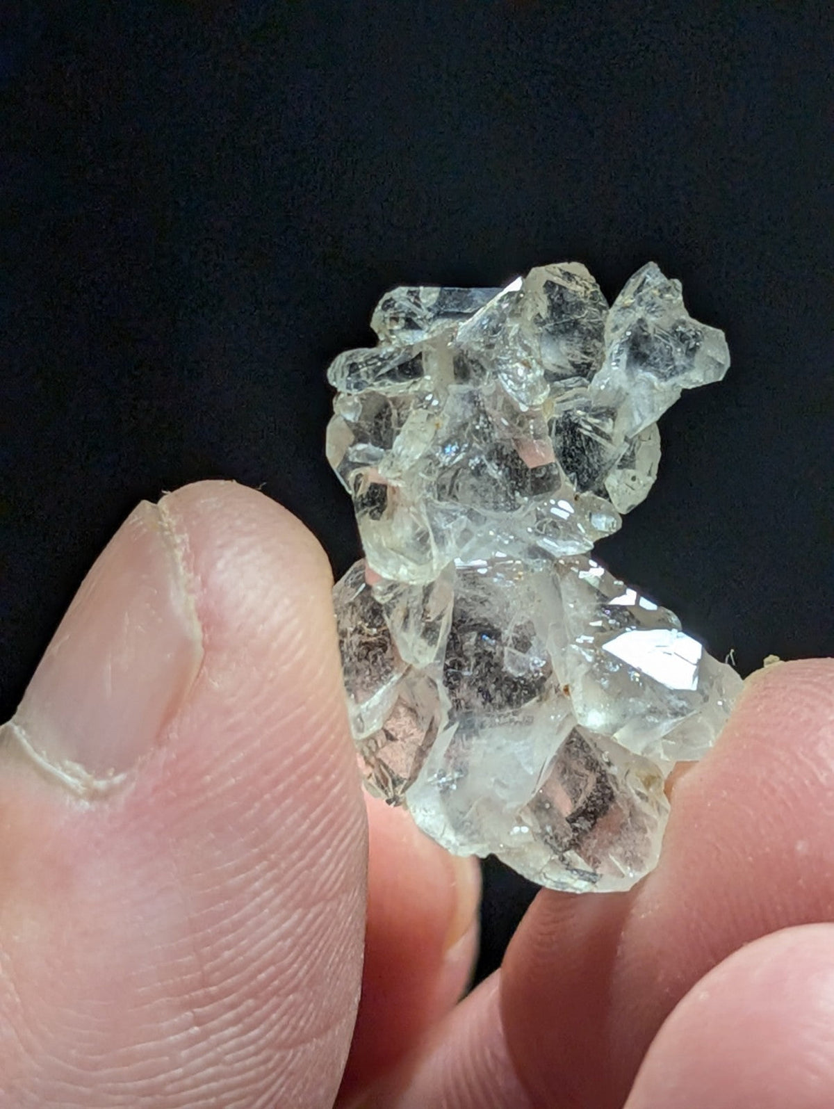 A cluster of clear, faceted quartz crystals held between fingers.