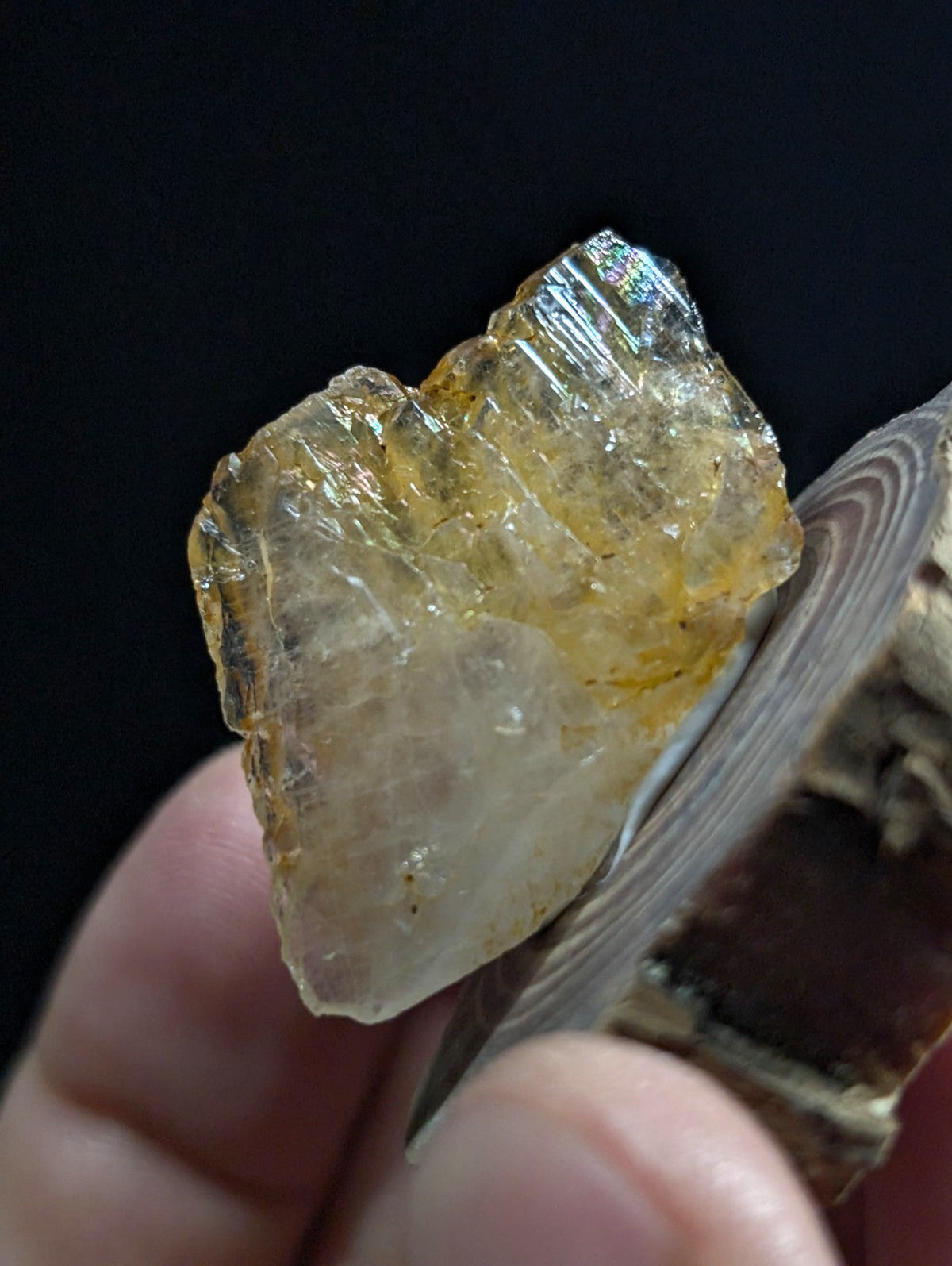 A translucent yellowish crystal with visible internal striations and a slightly iridescent sheen, held between fingers.