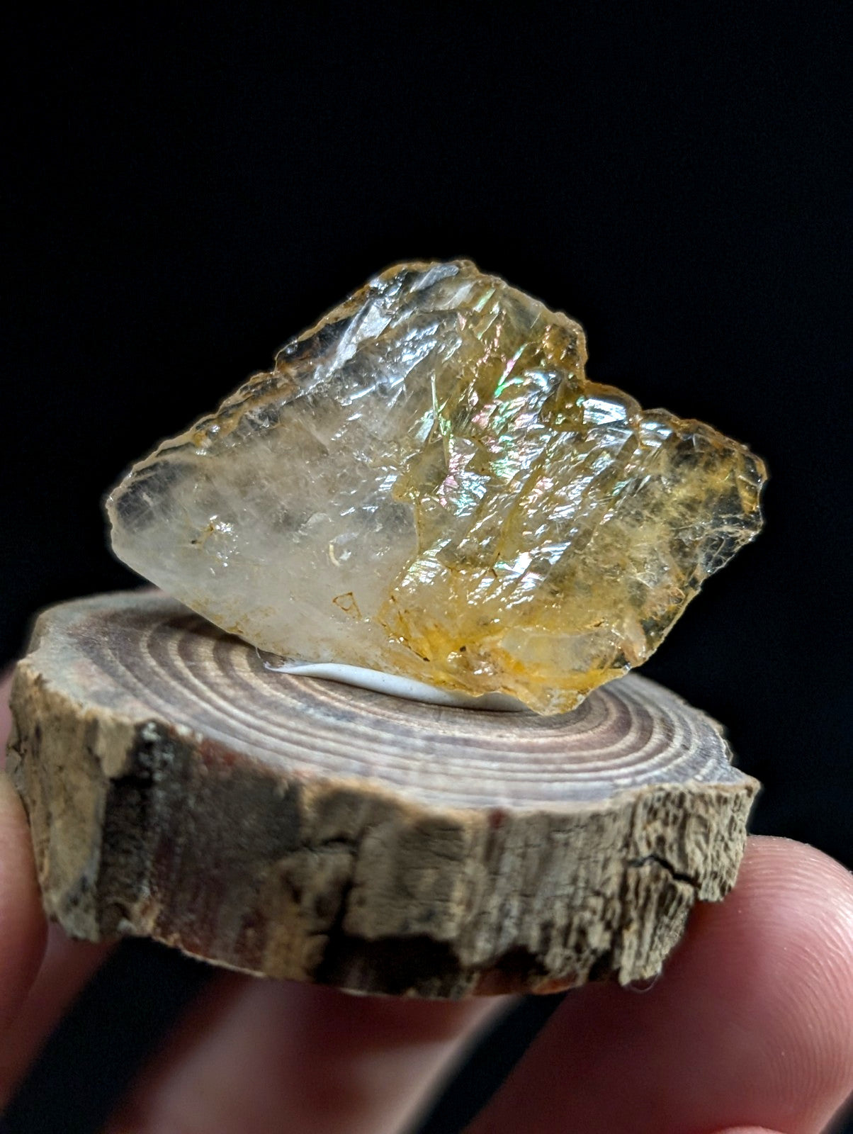 A translucent yellowish crystal with a rough, jagged surface rests on a circular wooden slice.