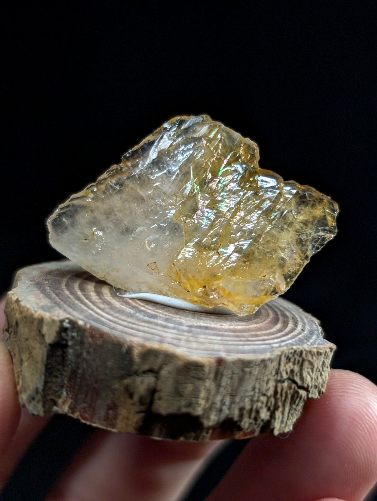A translucent yellowish crystal with a rough, jagged surface rests on a circular wooden slice.