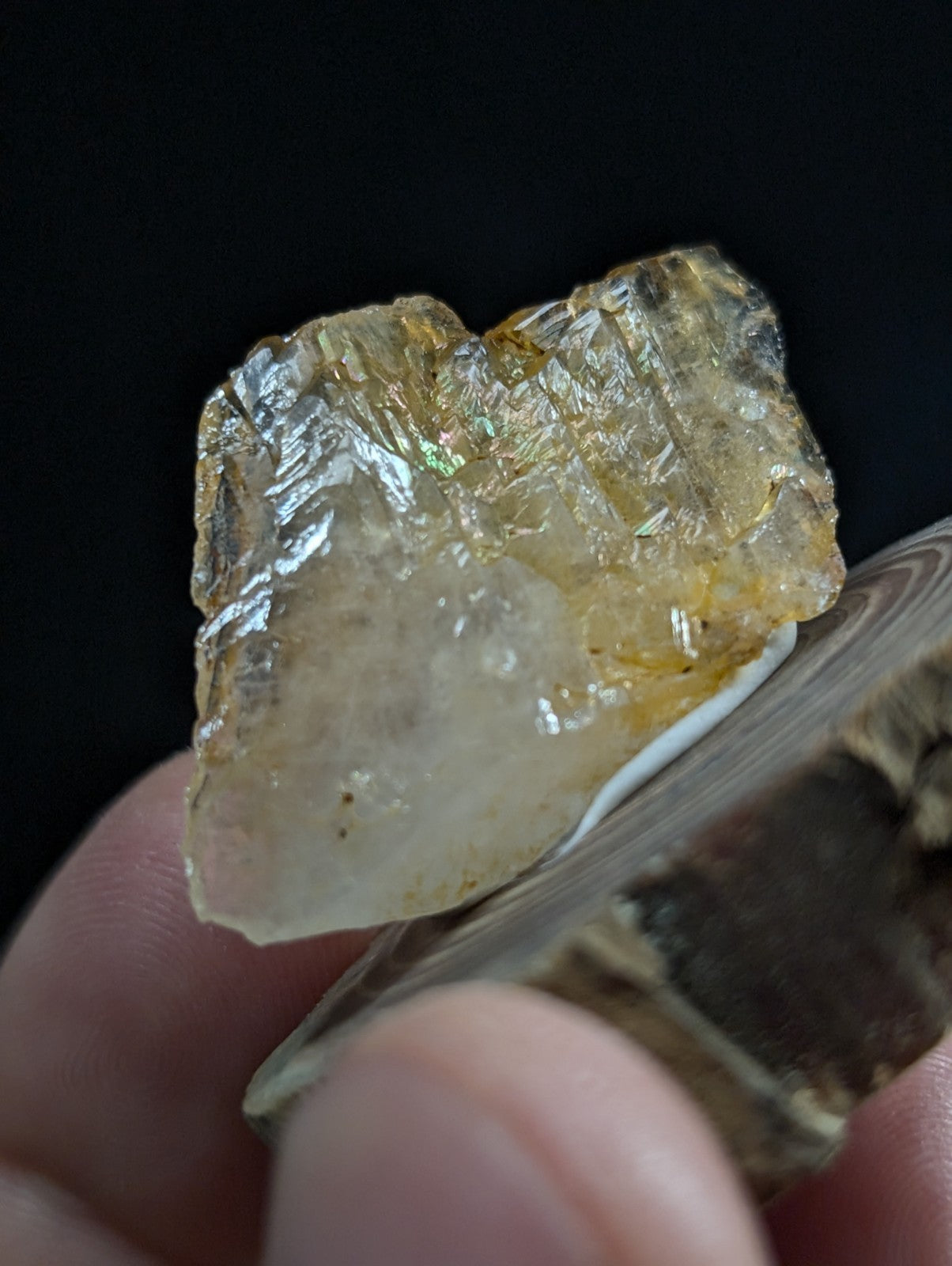 A translucent yellowish crystal with a rough, faceted surface and subtle iridescent flashes.