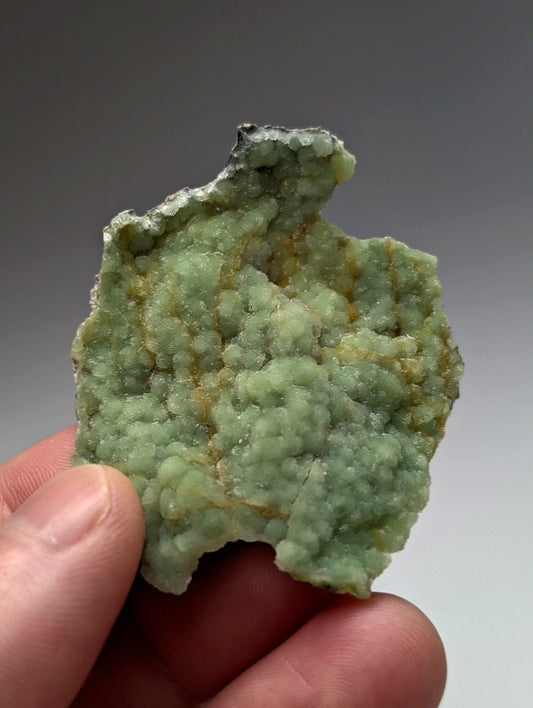 A hand holds a rough light green wavellite cluster with crystalline texture and yellowish inclusions from Arkansas USA