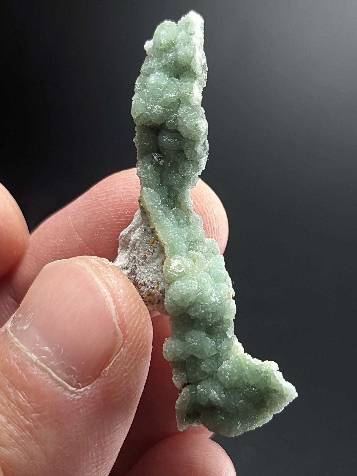 A delicate, light green mineral specimen with a textured, crystalline surface and subtle white veining.