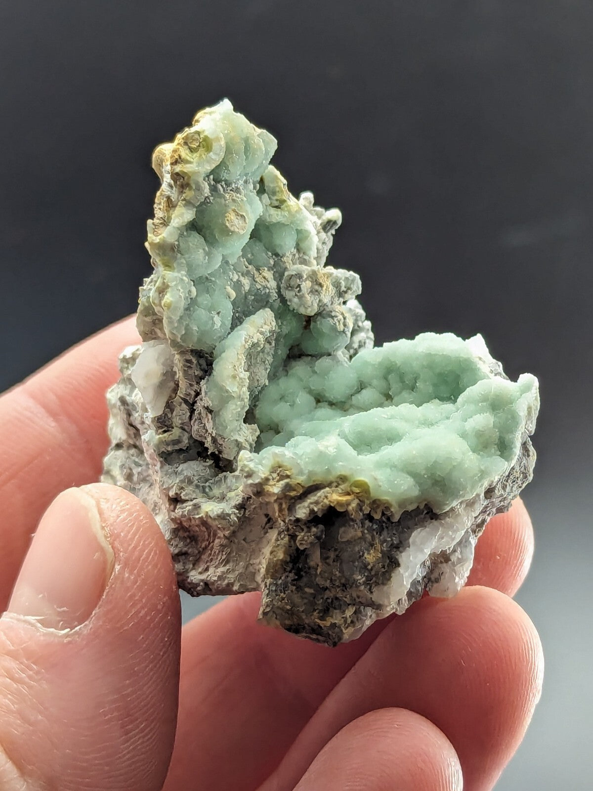 A delicate, pale green mineral specimen with a textured, crystalline surface and hints of yellowish tones.