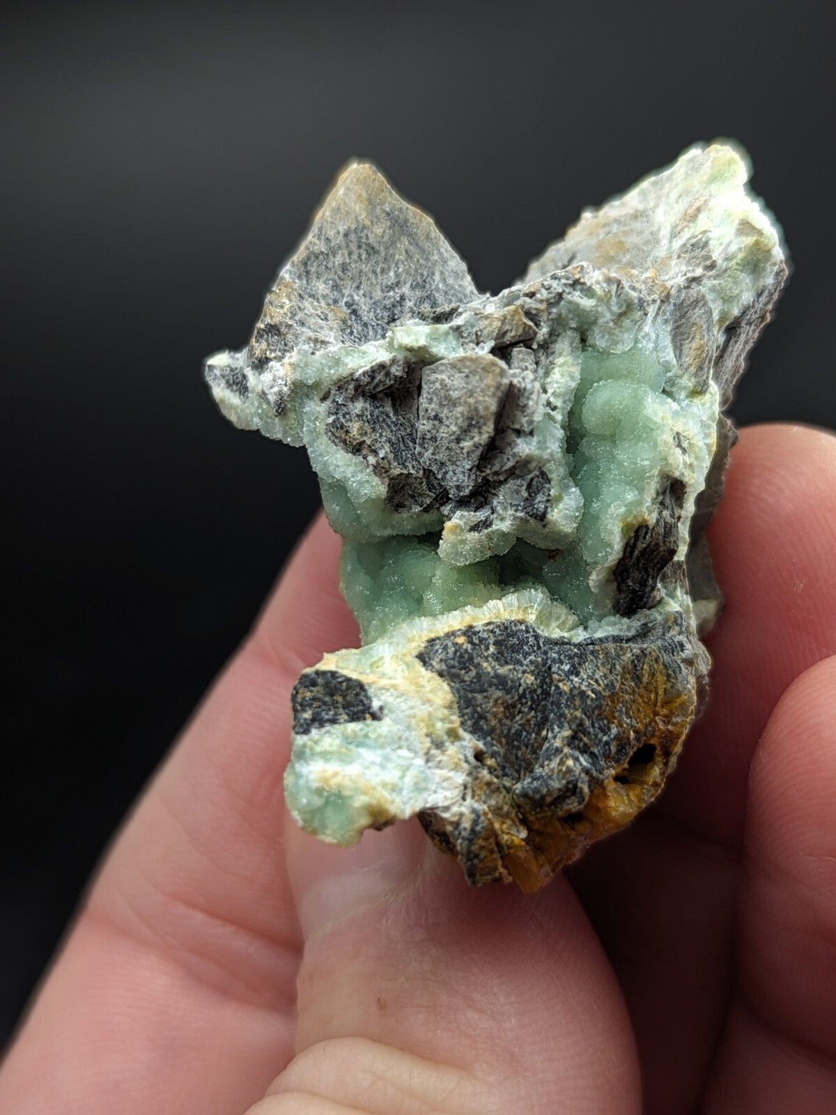 A rough, irregularly shaped mineral specimen with a translucent light green crystalline core surrounded by darker gray and yellowish matrix material.