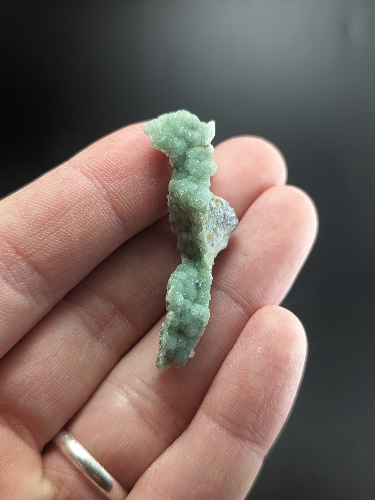 A delicate, light green mineral specimen with a textured, crystalline surface and subtle hints of gray.