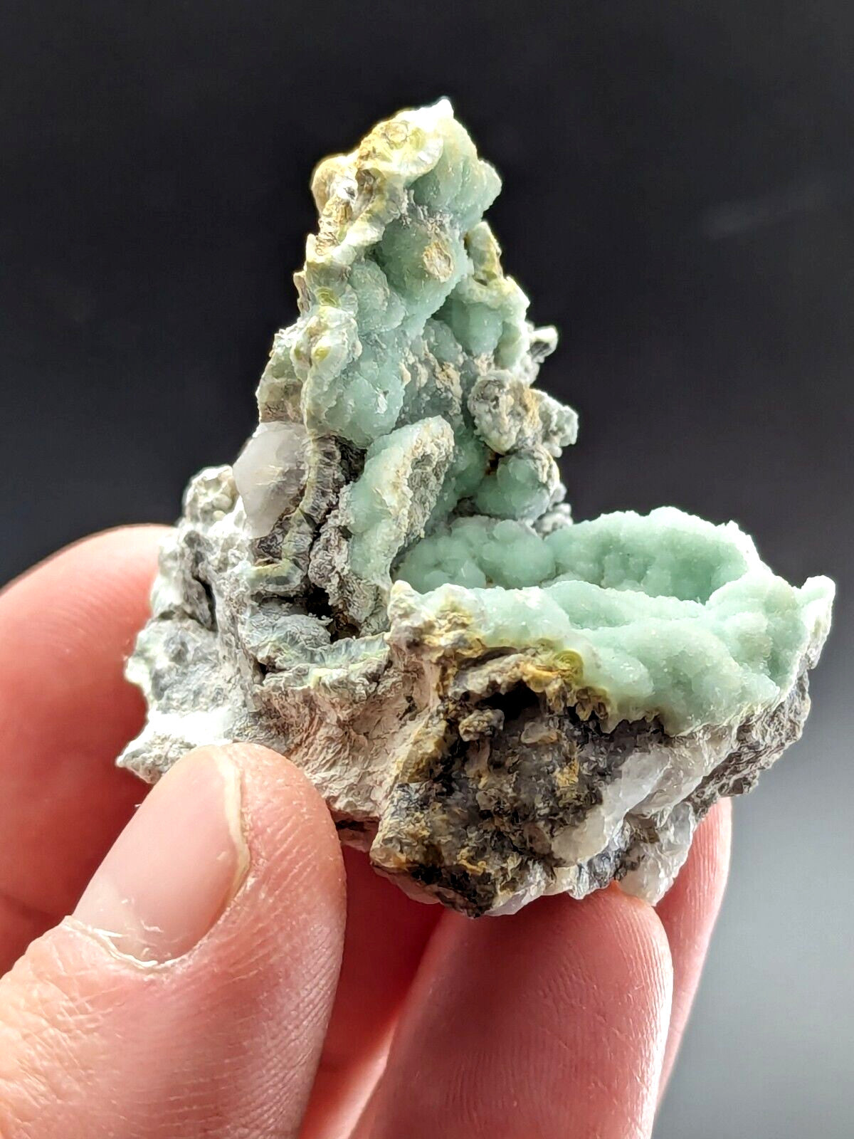 A delicate, light green mineral specimen with a crystalline texture and earthy gray matrix.
