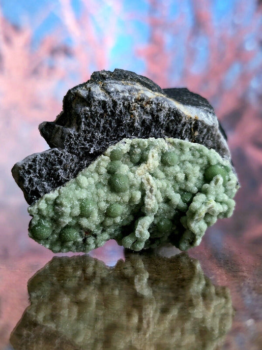 A striking green mineral specimen with a textured, bumpy surface and dark gray rock base.