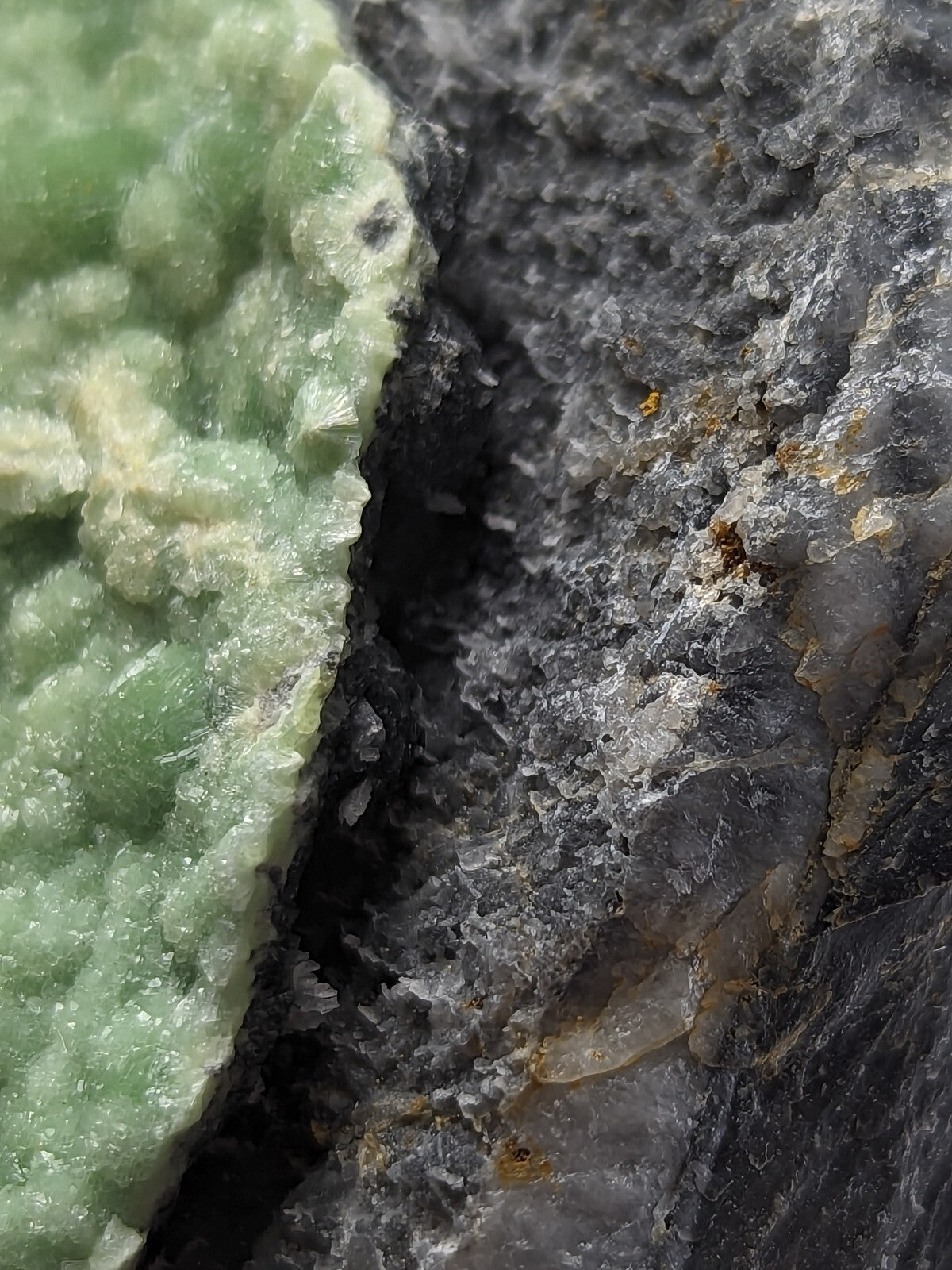 A textured green mineral formation juxtaposed against a dark, crystalline rock surface.
