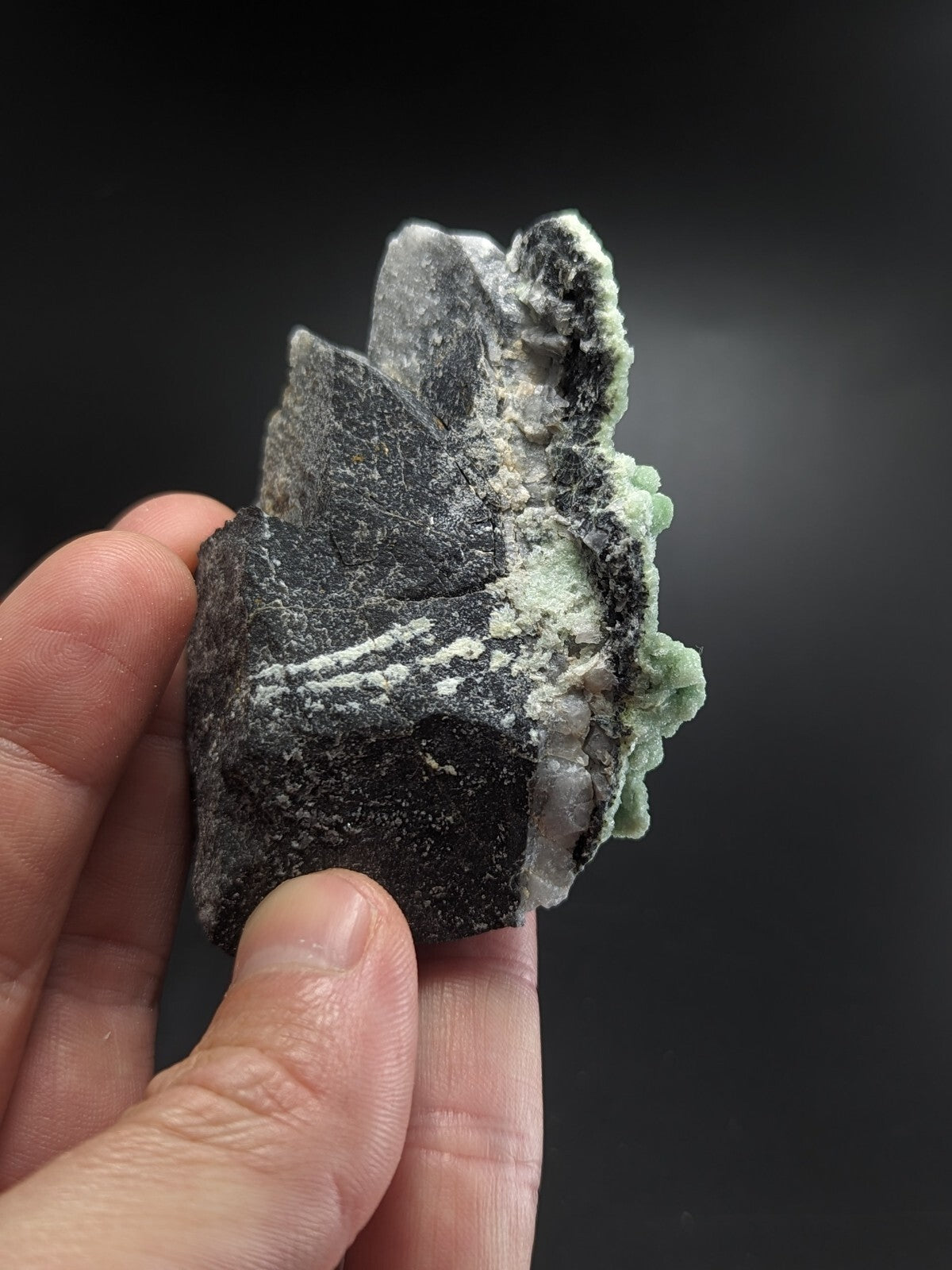 A striking black and green mineral specimen with a rough, textured surface featuring crystalline formations.