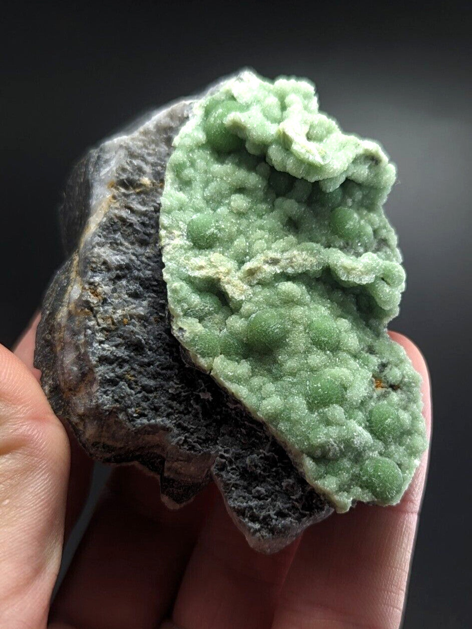 A hand holds a striking green mineral specimen with a textured, bumpy surface against a dark background.