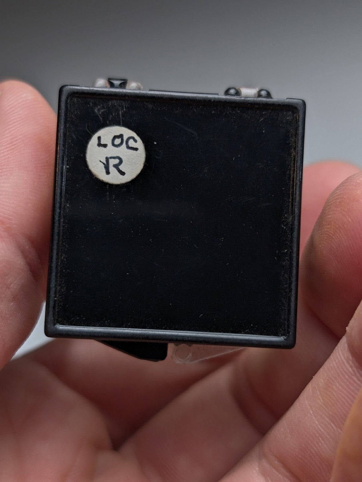 Black rectangular electronic component with white circular sticker labeled loc r on top unique wavellite near turquoise