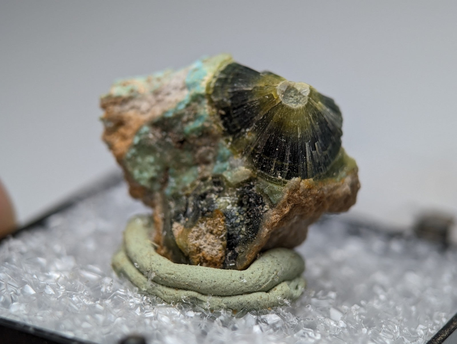 Unique wavellite mineral specimen with a glossy green and black crystalline surface on a light gray clay base from Arkansas