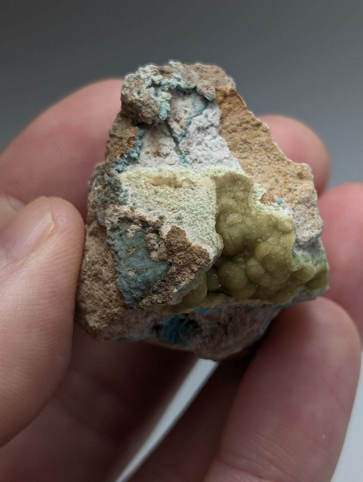 A hand holds unique wavellite with greenish blue and yellow green crystals on tan matrix from Garland County Arkansas