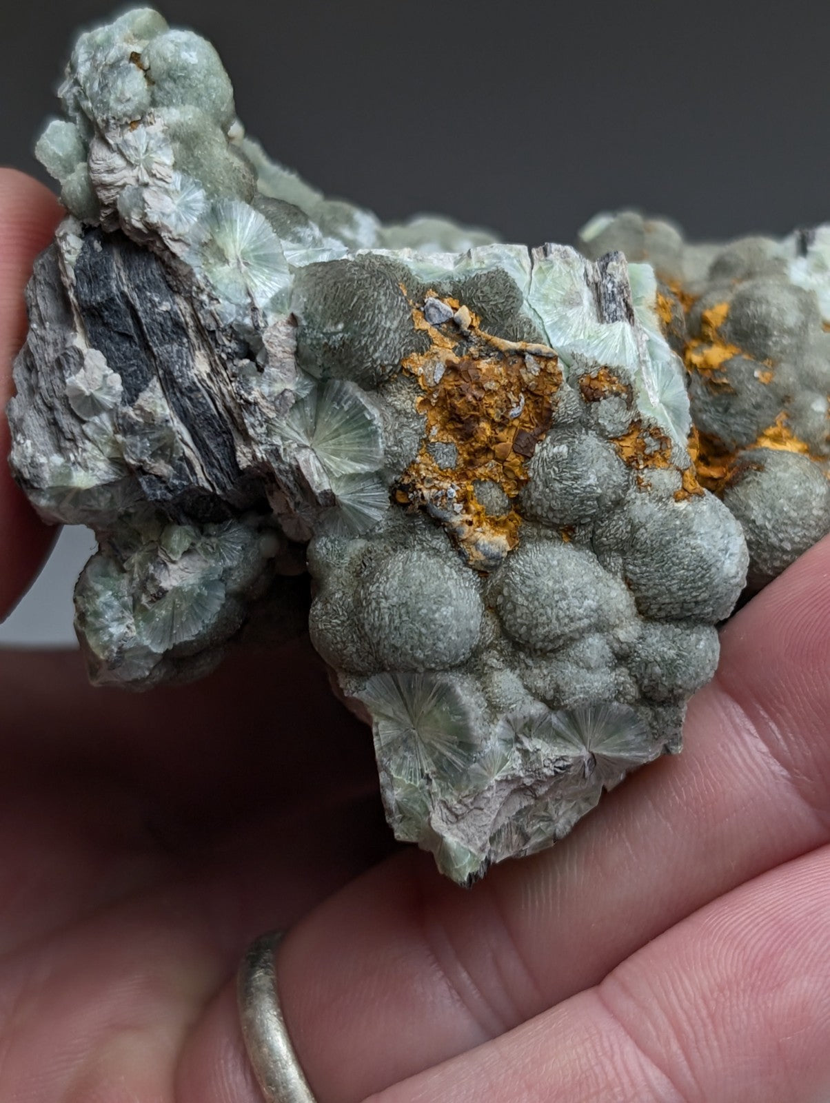 A hand holds a uv reactive green wavellite cluster with pale green crystals and orange rust from Mauldin Mountain Arkansas