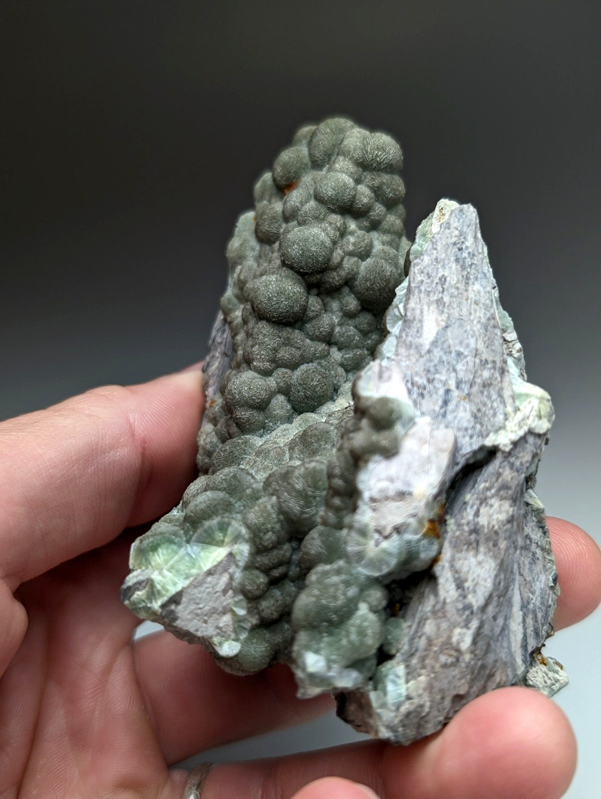 A hand holds a uv reactive green wavellite cluster with bubble formations on gray matrix from Mauldin Mountain Arkansas
