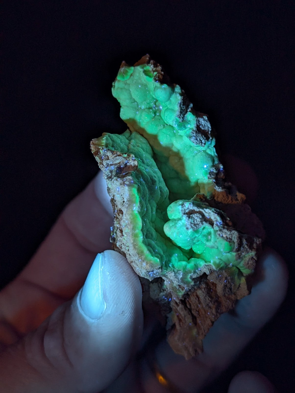 A glowing green fluorescent mineral specimen with a rough, textured surface and earthy brown matrix.