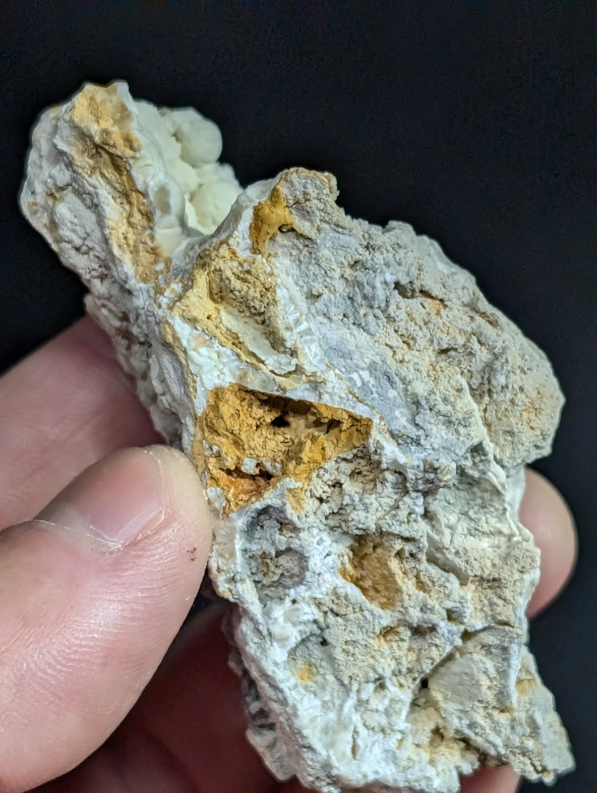 A rugged, irregularly shaped rock with a textured surface featuring patches of white and golden-yellow mineral deposits.