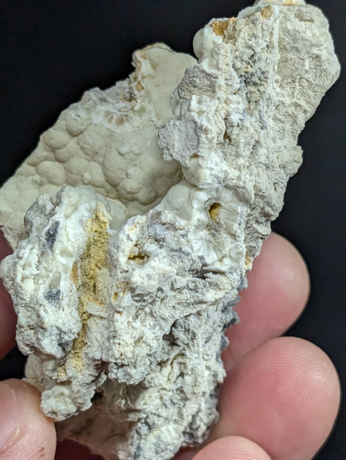 A textured, irregularly shaped mineral specimen with a predominantly white and gray surface accented by streaks of yellowish-brown.