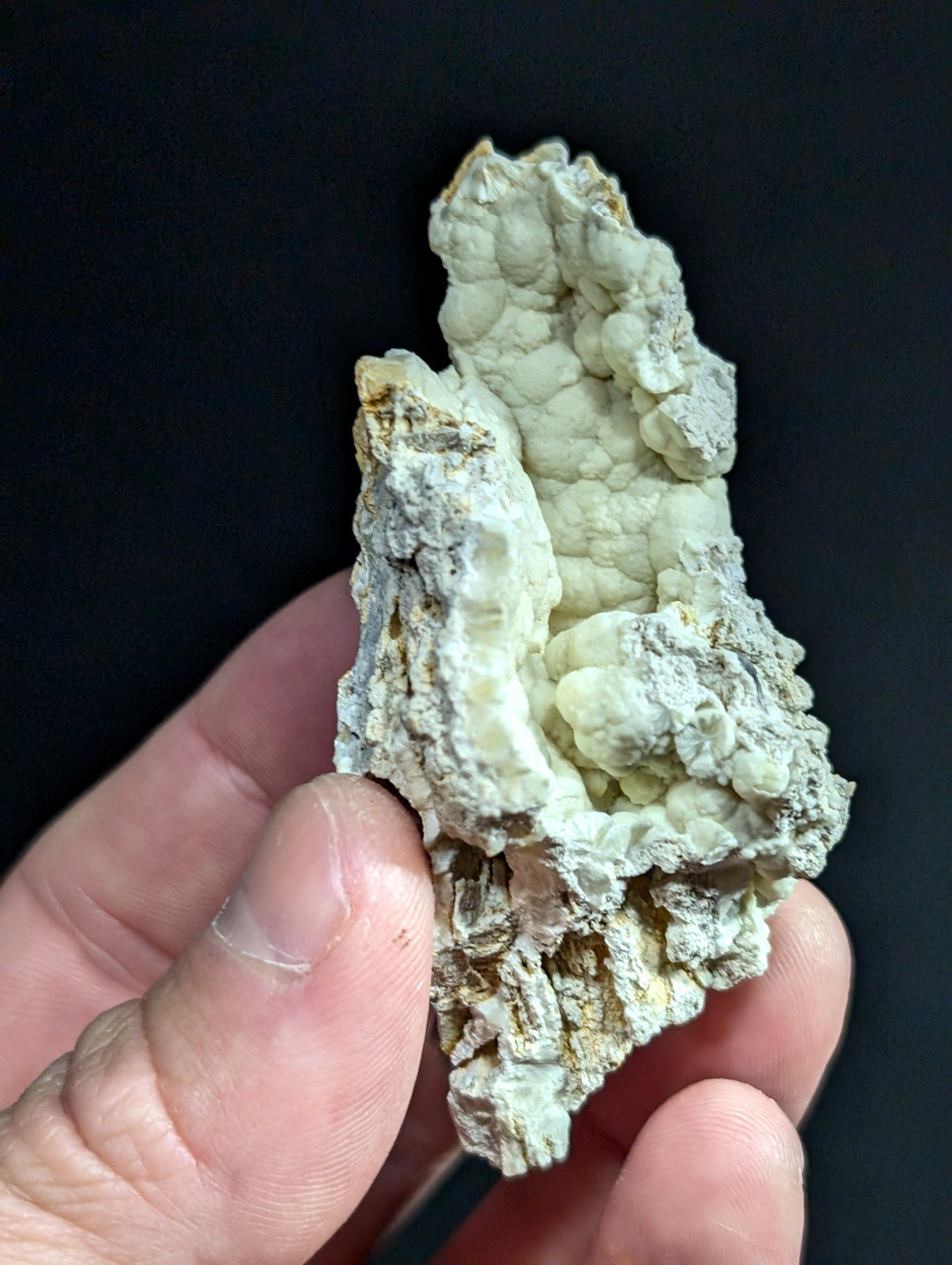 A textured, pale greenish-white mineral specimen with a rough, bumpy surface and subtle yellowish-brown patches.