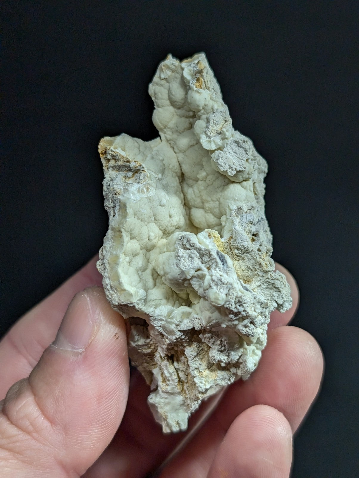 A pale greenish-white, rough-textured mineral specimen with subtle yellow and gray patches.