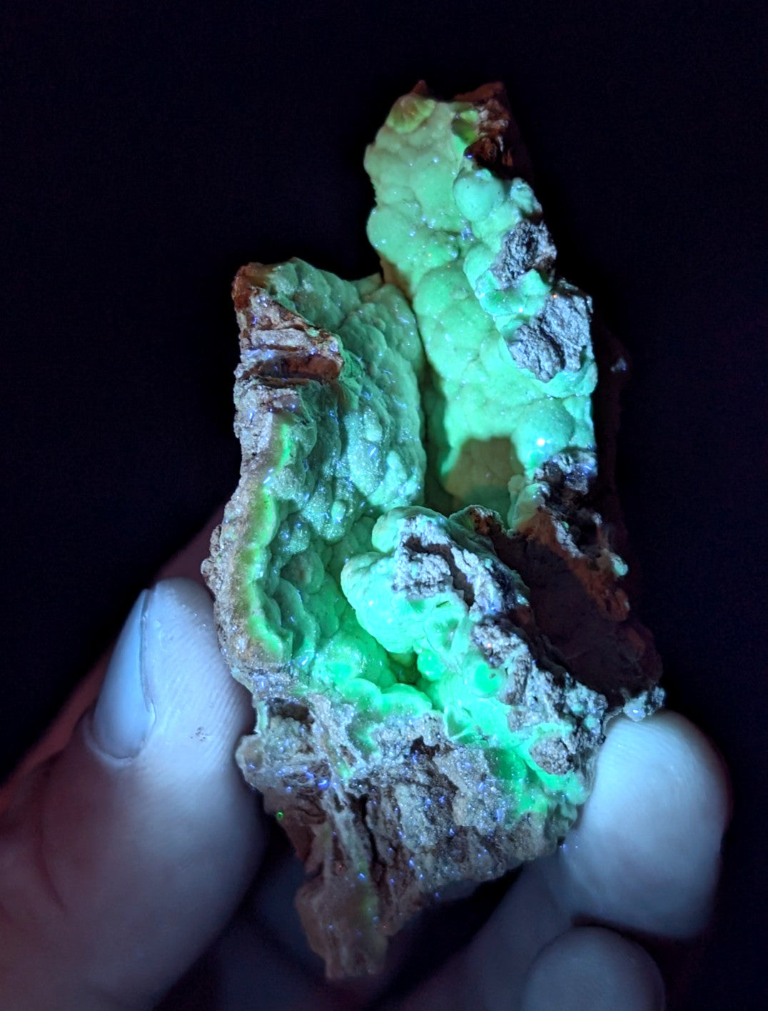 A glowing green mineral specimen with a rough, textured surface and earthy brown matrix.