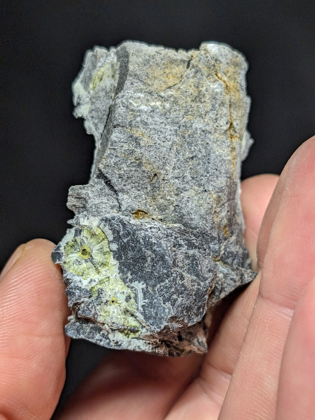 A rough, irregularly shaped rock with a grayish surface and patches of green mineral growth.