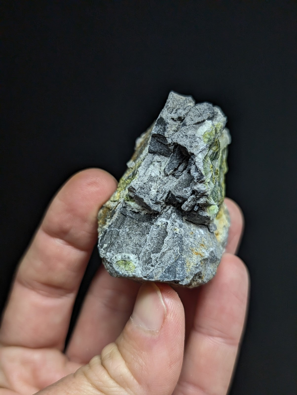 A rugged, irregularly shaped rock with a mottled gray surface accented by patches of green and yellow mineral veins.