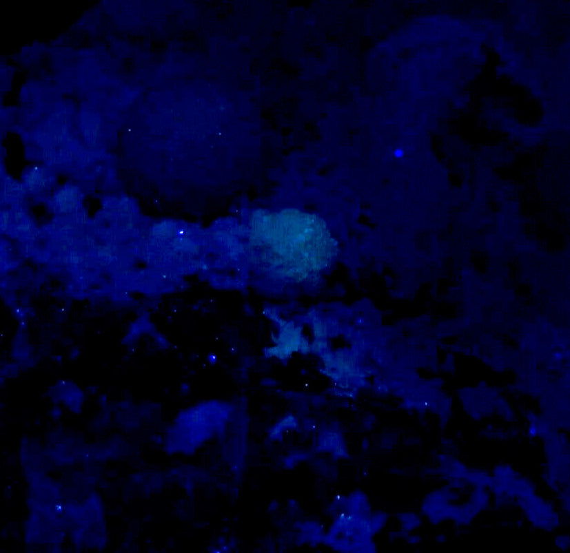 A glowing blue mineral specimen with a textured, uneven surface and scattered luminescent specks.