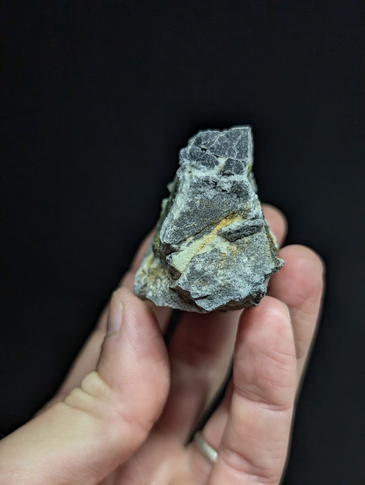 A rough, irregularly shaped gray rock with patches of yellow mineral streaks held in a hand.