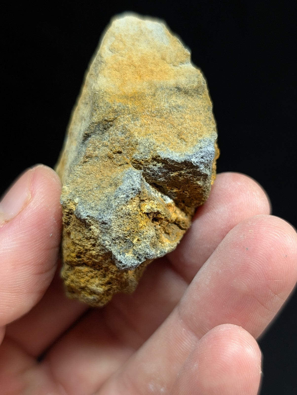 A rough, irregularly shaped mineral specimen with a mottled surface of golden-yellow and bluish-gray patches.
