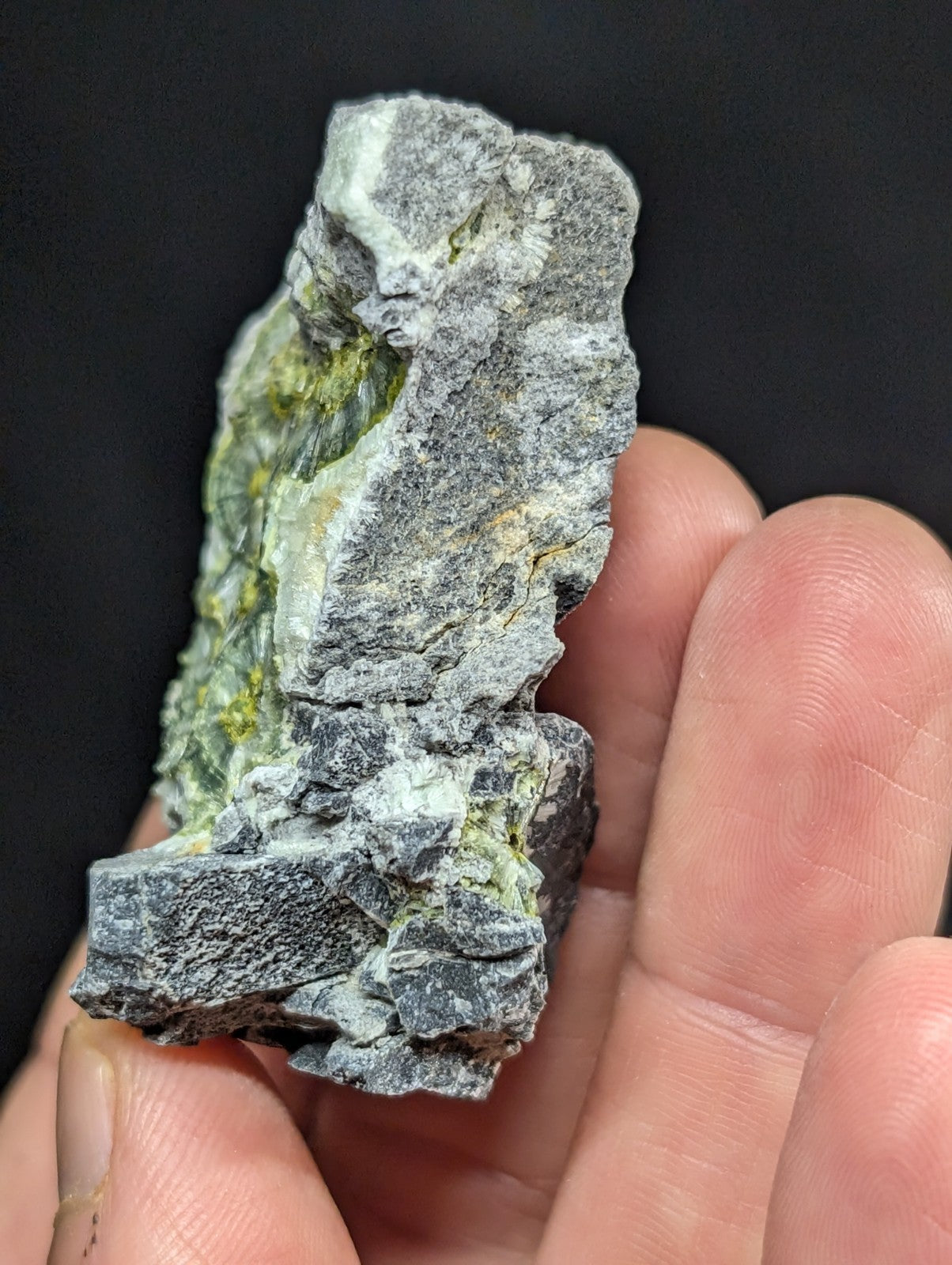 A rough, irregularly shaped mineral specimen with a grayish base and patches of greenish-yellow veining.