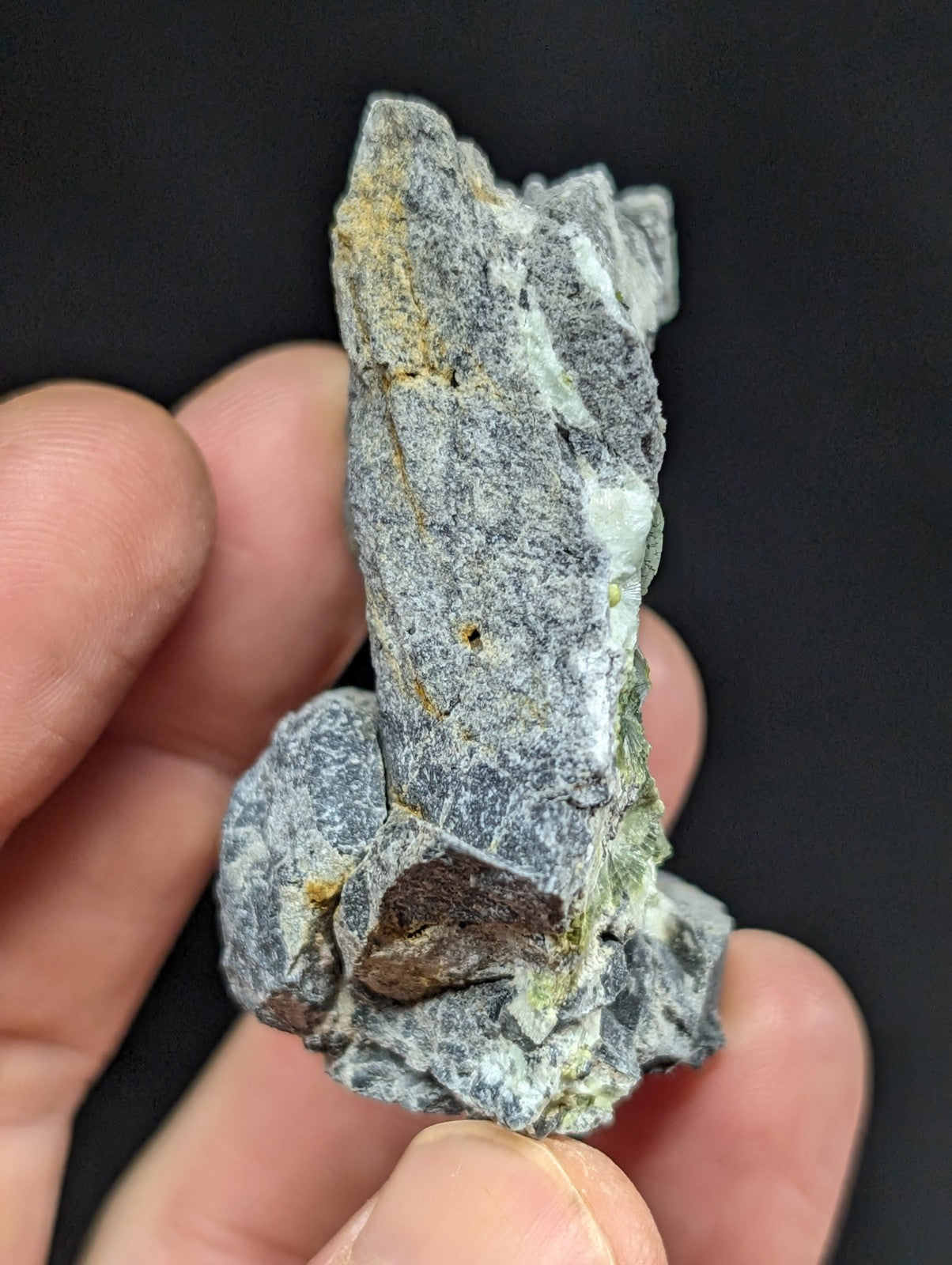 A rugged, grayish rock specimen with patches of yellow and brown mineral inclusions.