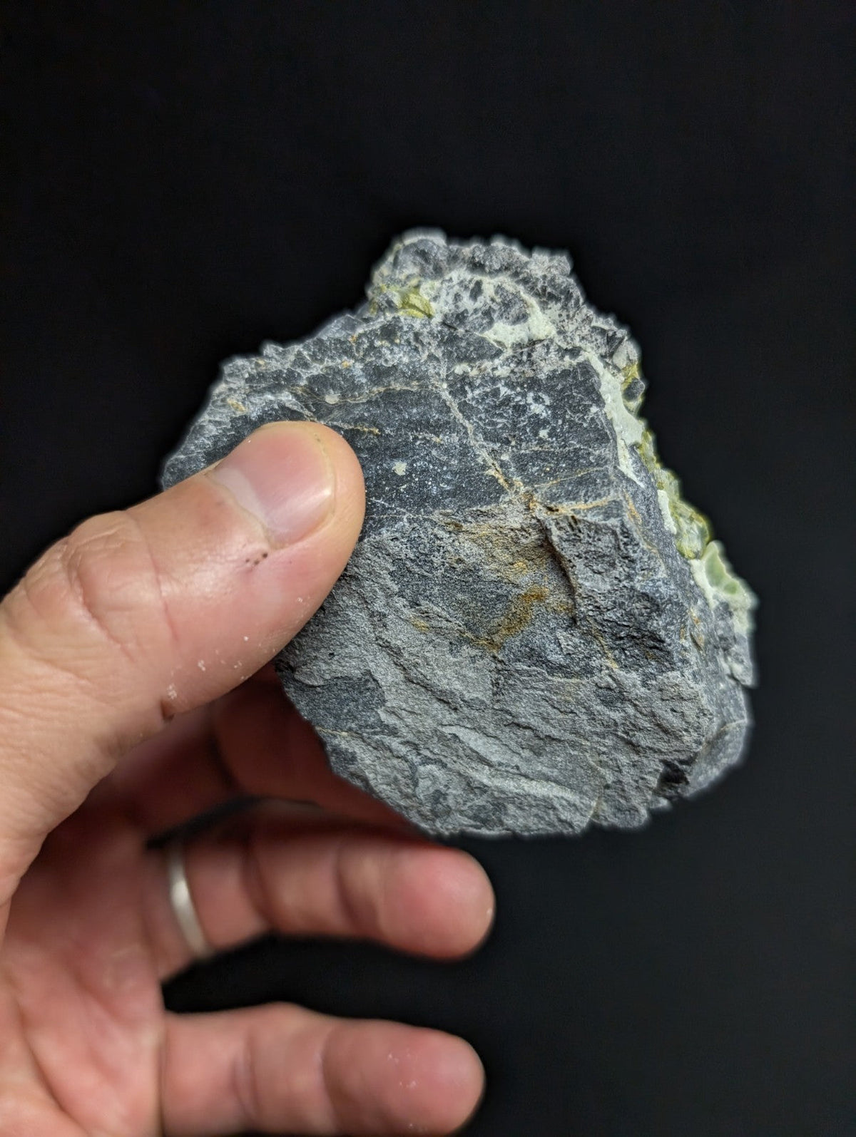 A rough, irregularly shaped gray rock with subtle greenish-yellow mineral veins and a textured surface.