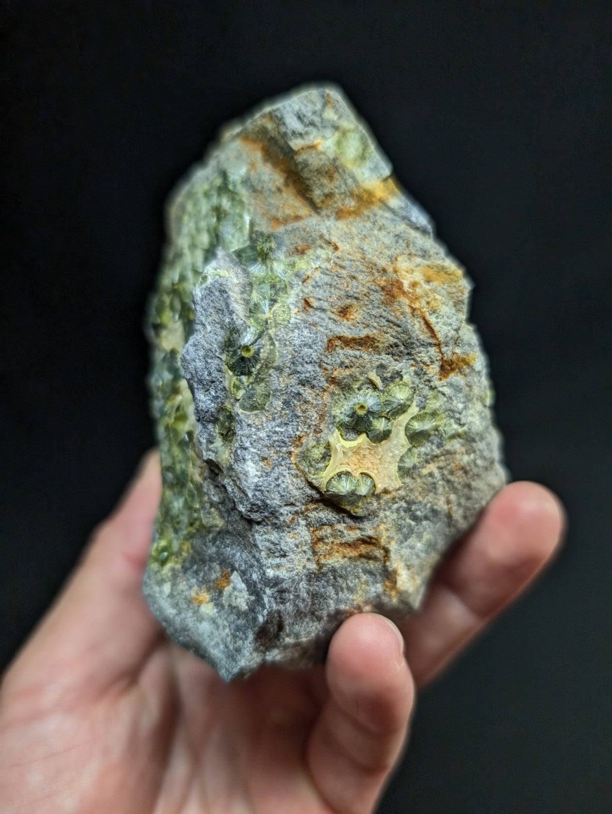 A rugged, irregularly shaped rock with a mottled gray surface accented by patches of green and orange mineral veins.