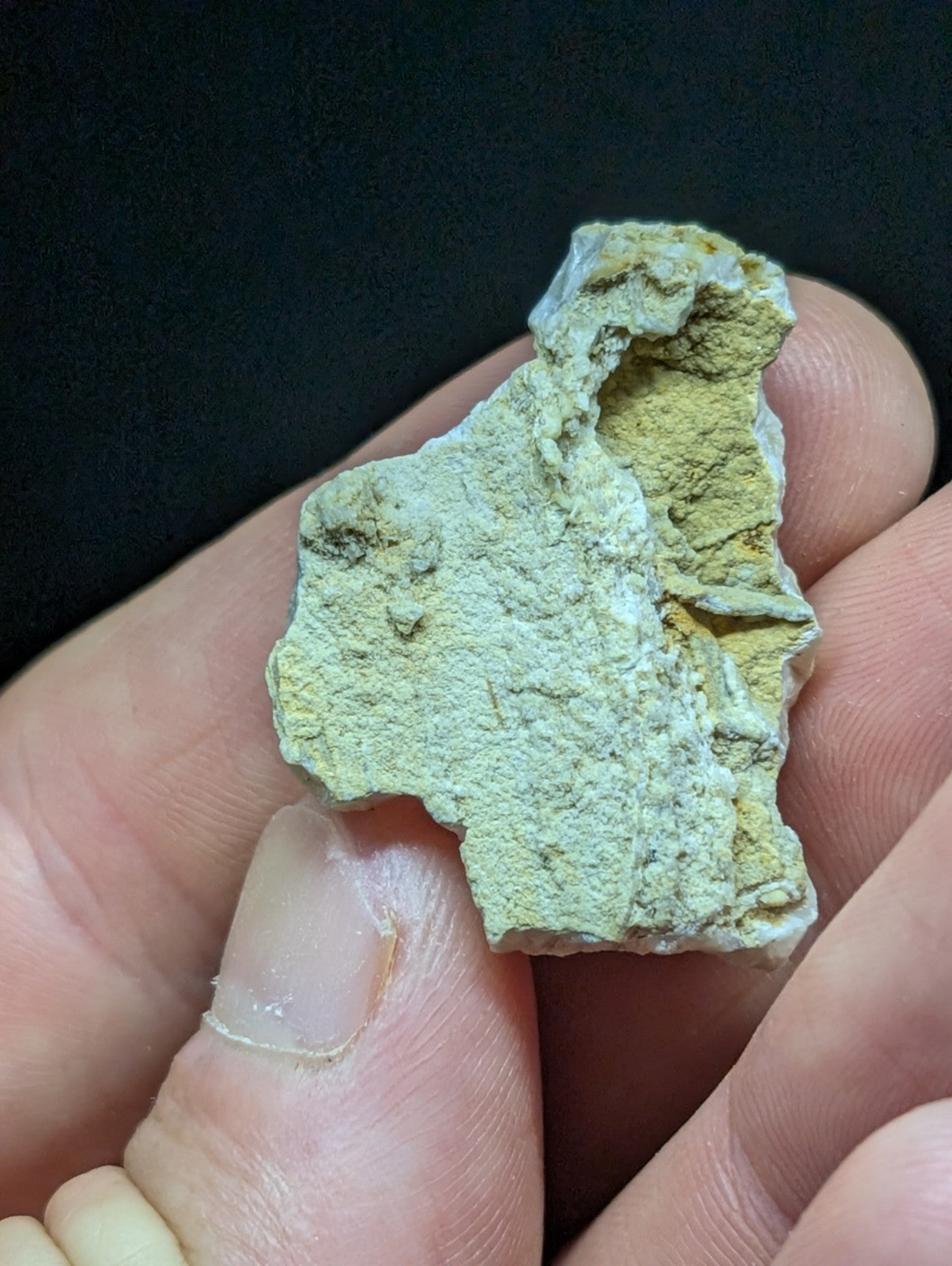 A rough, irregularly shaped mineral specimen with a pale greenish-yellow surface and visible crystalline texture.
