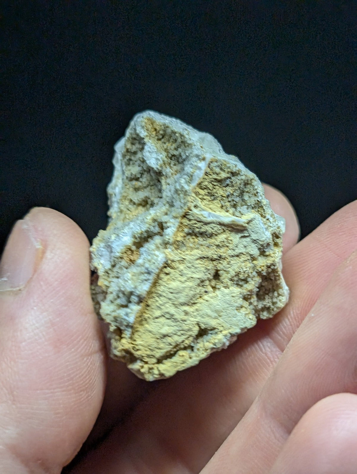 A rough, irregularly shaped mineral specimen with a mottled surface of pale yellow and grayish-white hues.
