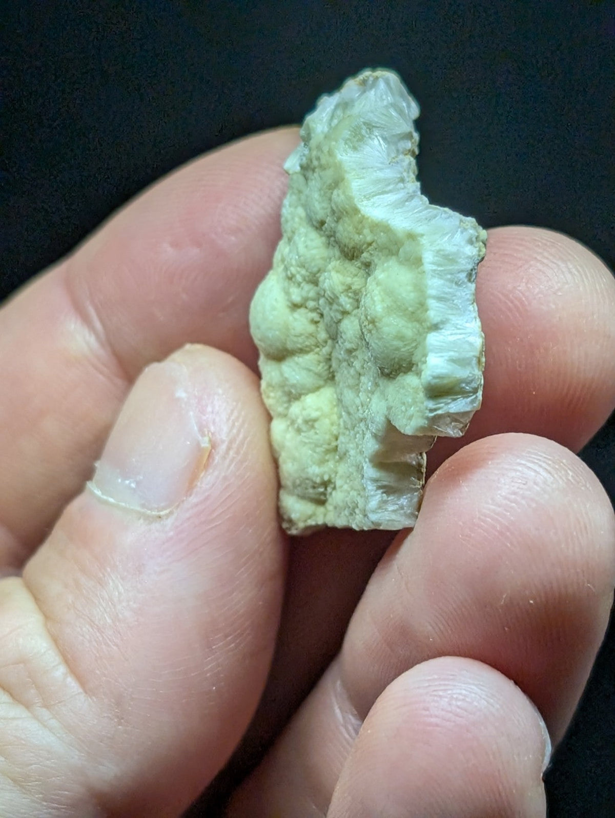 A pale green, rough-textured mineral specimen with a jagged edge and layered internal structure.