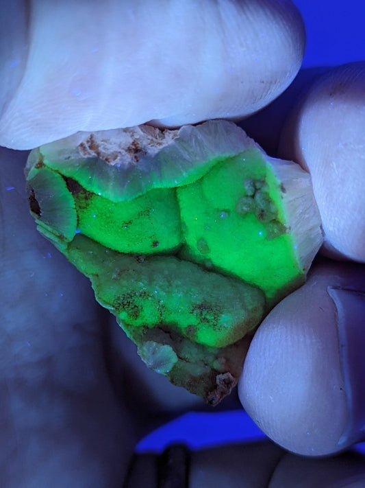 A glowing green fluorescent mineral specimen with a rough, irregular surface and natural earthy matrix.