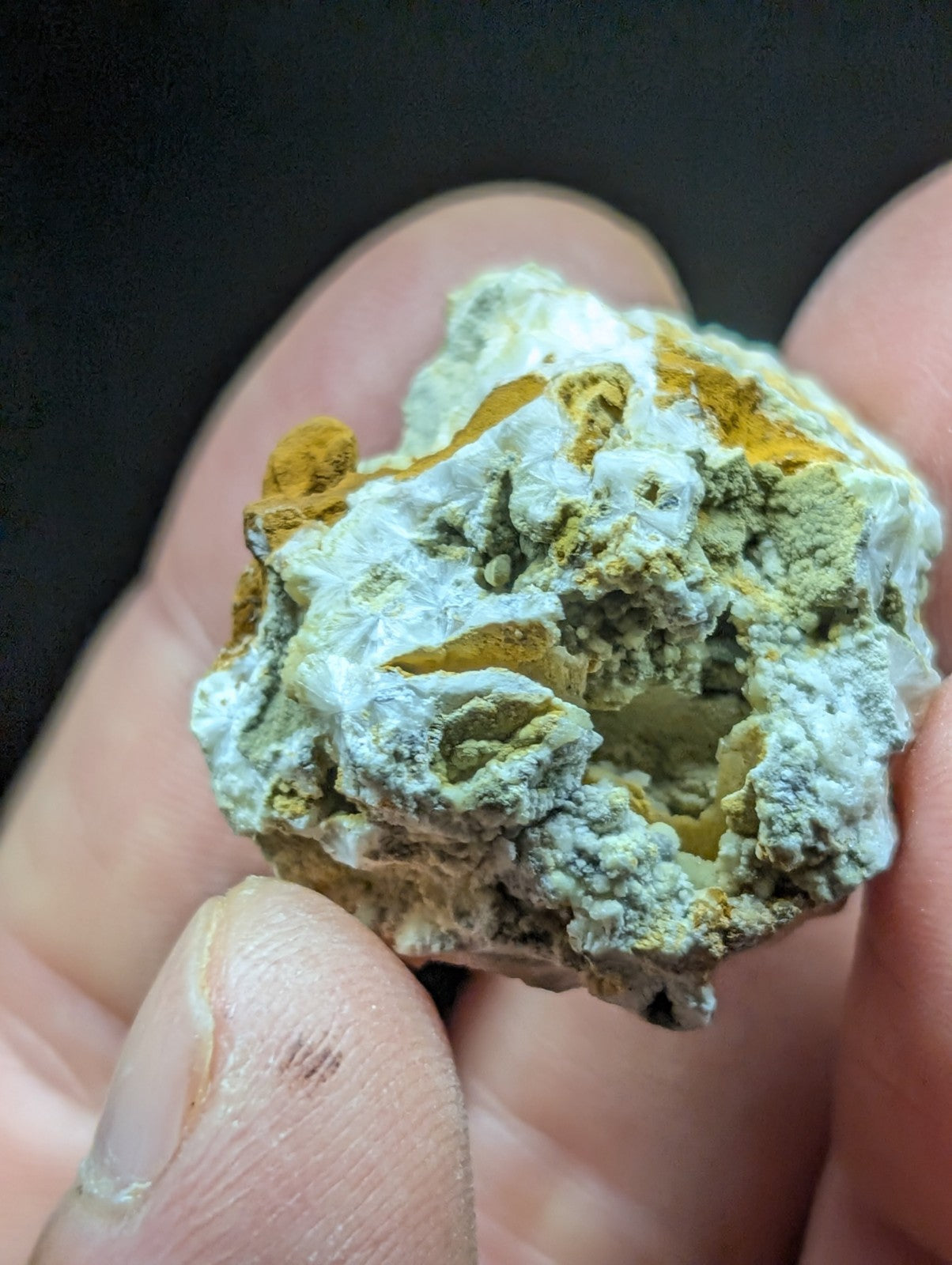 A rough, irregularly shaped mineral specimen with a textured surface featuring patches of white and yellowish-green hues.