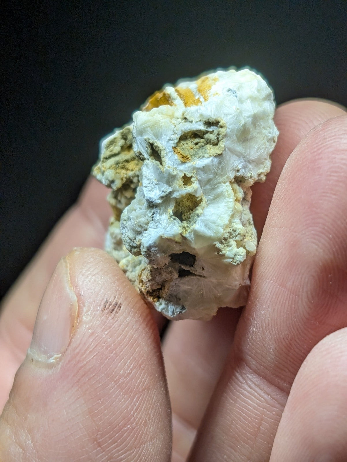 A rough, irregularly shaped mineral specimen with a predominantly white base and patches of yellowish-orange and greenish hues.