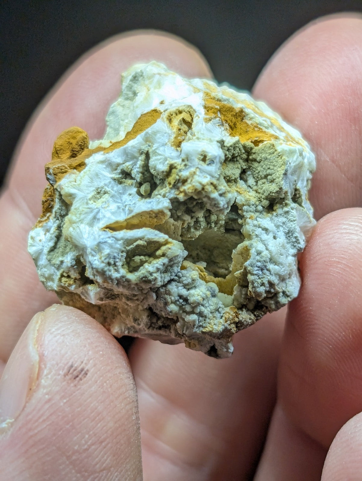 A rugged, irregularly shaped mineral specimen with a textured surface displaying patches of white and yellowish-green hues.