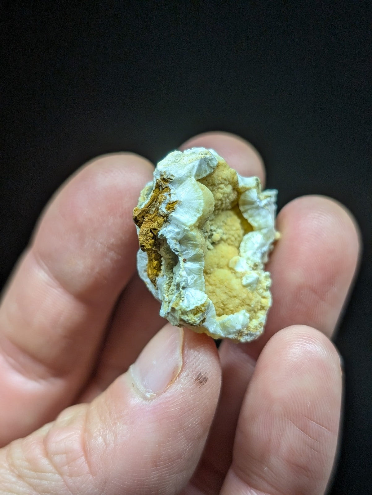 A hand holds a small, irregularly shaped geode with a pale blue-green crystalline exterior and a golden-yellow interior.