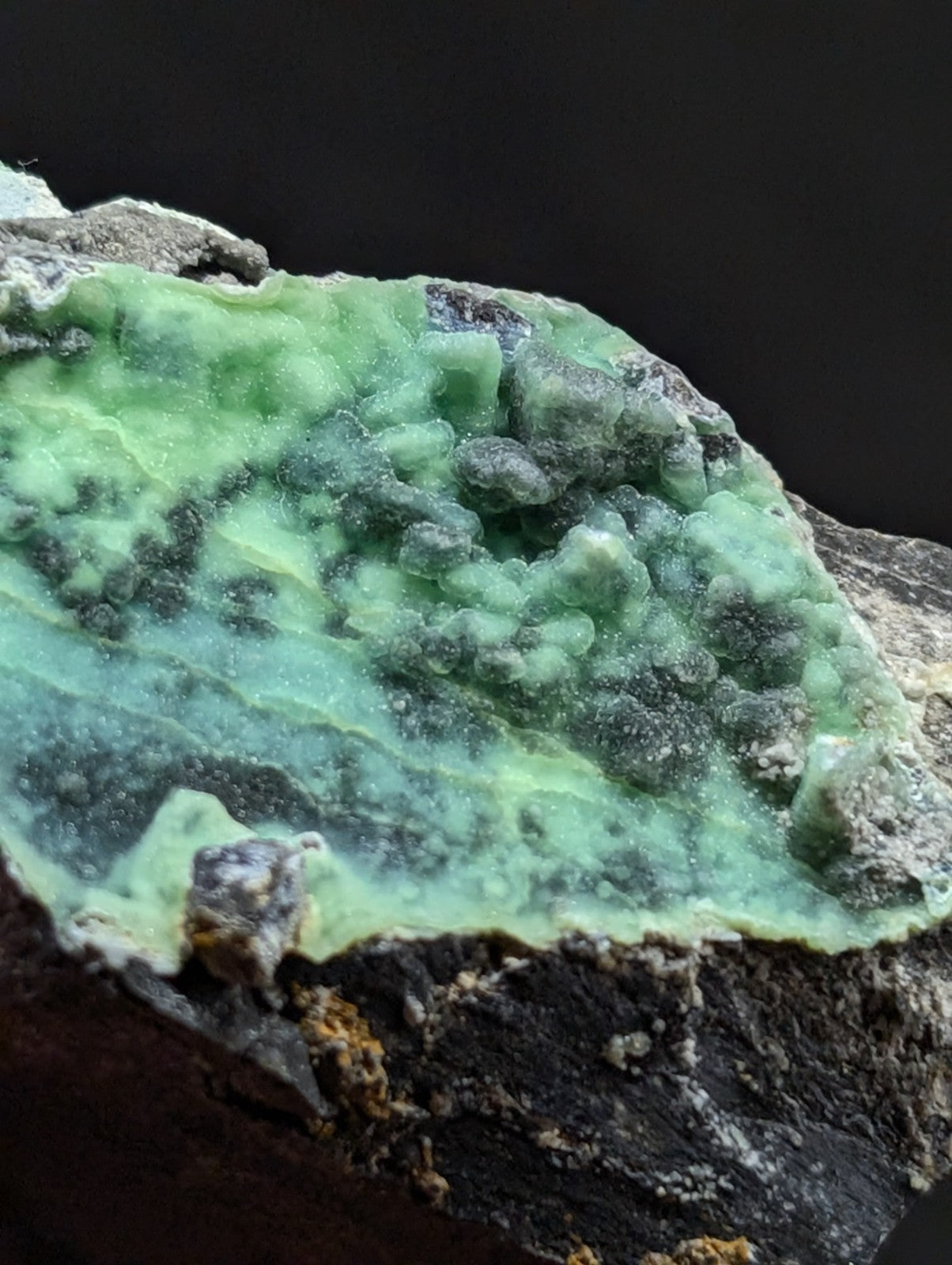 A vibrant green, translucent mineral specimen with a textured surface and dark speckles embedded in its crystalline structure.
