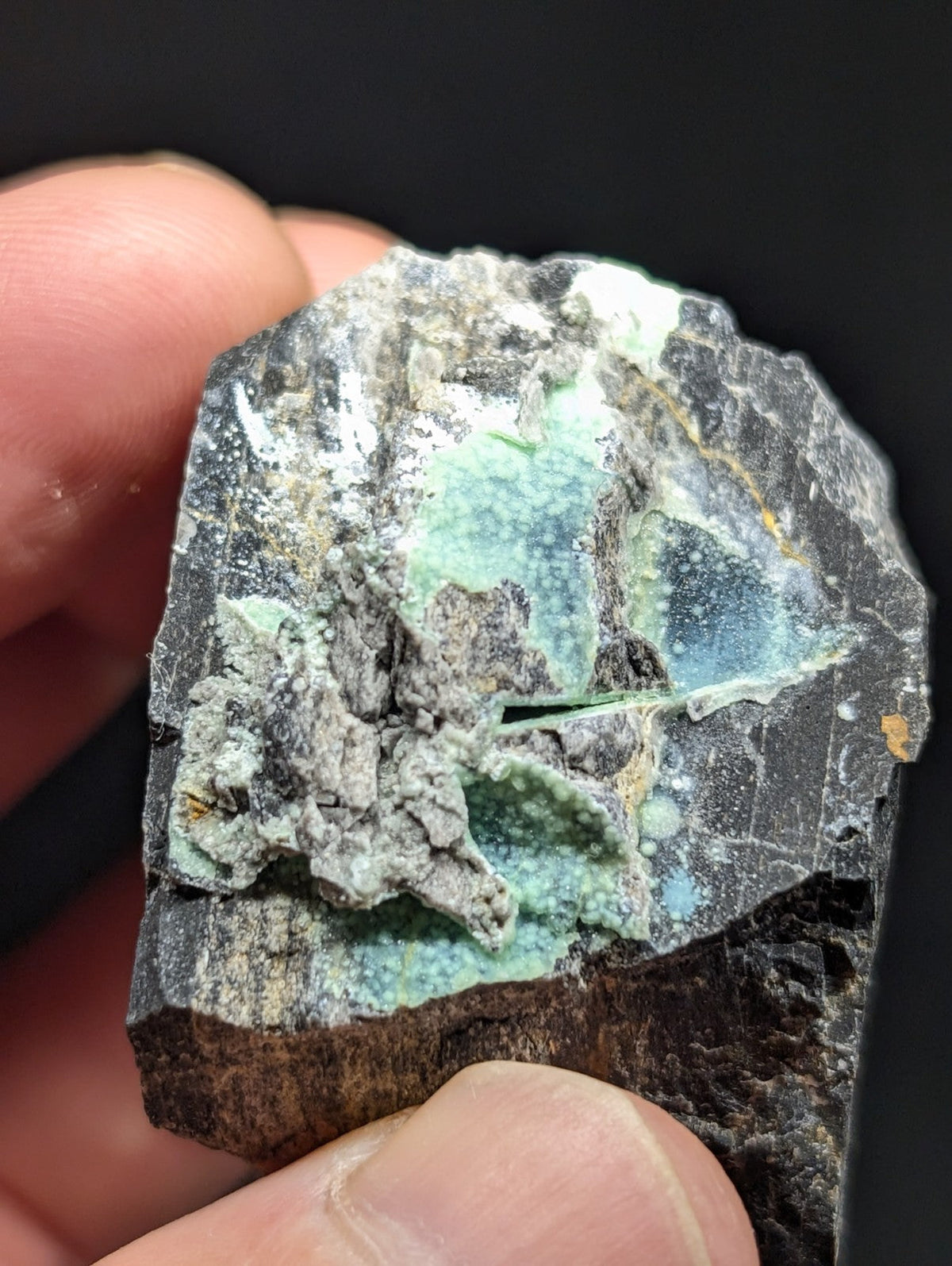 A rough, irregularly shaped mineral specimen with a dark gray matrix and vibrant turquoise-green veining.